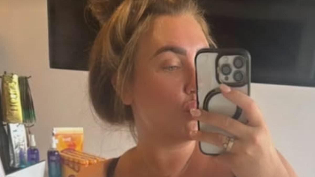 Lauren Goodger showcases her incredible curves in a plunging black tank top and grey shorts as she poses for selfies at the beauty salon