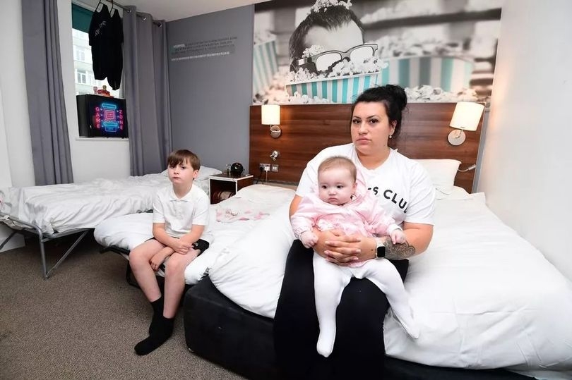 The mum and two kids living in a hotel room with beds pushed together