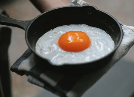 Teacher fries egg in pan on hot French school playground floor